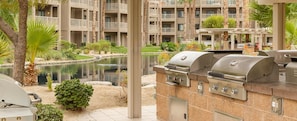 Une terrasse avec un barbecue, un petit étang et un bâtiment doté de balcons.