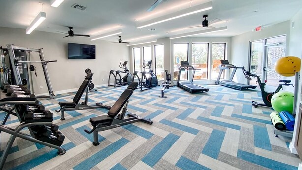 A gym with various exercise equipment, large windows, and a patterned floor. - Landing | Modern 1BD, Gym, Clubhouse (Fort Worth)