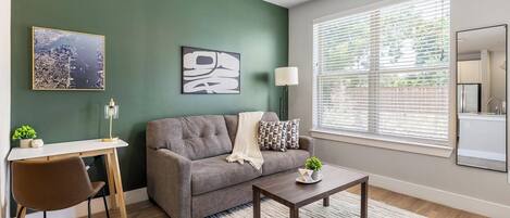 A living room with a grey sofa, a coffee table, a desk with a chair, a lamp, and artwork on the walls.