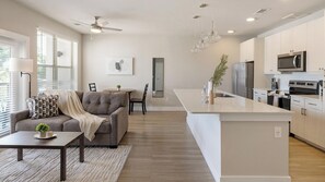 A modern kitchen with a central island, stainless steel appliances, and a dining area with a sofa and table. - Landing | Stunning 1BD, Clubhouse, Gym (Fort Worth)