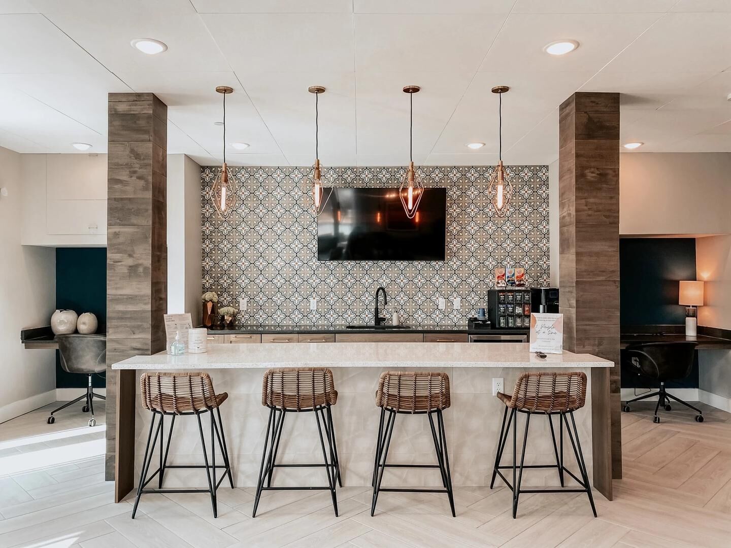 A modern kitchen with a central island, bar stools, pendant lighting, and a flat-screen TV.