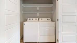 A laundry room with two white Whirlpool washers and dryers, a white door, and a white shelf above the dryers. - Landing | Spectacular 1BD, Clubhouse, Gym (Fort Worth)