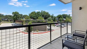 A balcony with a view of a parking lot and surrounding greenery. - Landing | Stunning 1BD, Clubhouse, Gym (Fort Worth)
