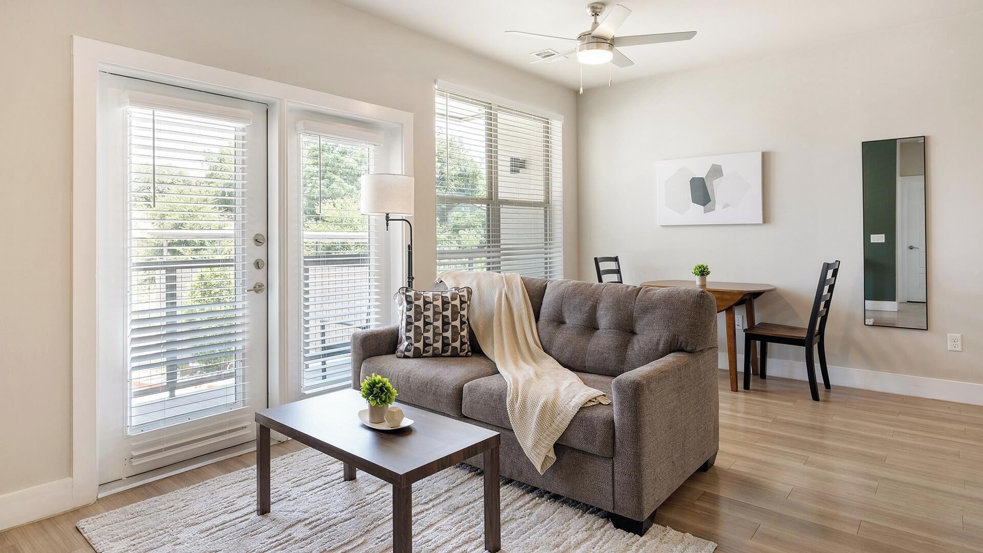 A living room with a sofa, a coffee table, a lamp, and a dining area with a table and chairs.