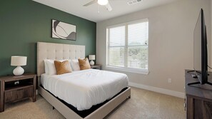 Ein Schlafzimmer mit einem großen Bett, einem Deckenventilator, einem Fenster mit Jalousien und einem Fernseher auf einem Schrank.
