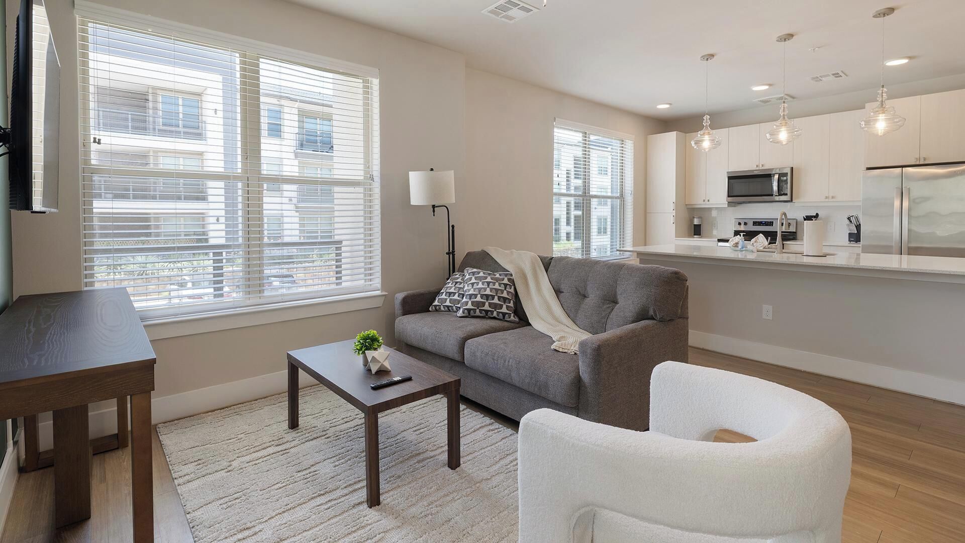 A modern living room with a sofa, a coffee table, and a chair. There is a kitchen area with a microwave and a refrigerator.