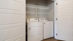 A laundry room with two stacked washers and dryers, white cabinetry, and a wooden floor.