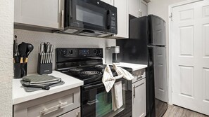 A compact kitchen with a stove, microwave, refrigerator, and a coffee maker. - Landing | Chic 2BD, Gym, Courtyard (Allen)