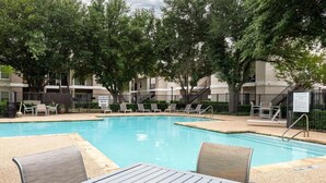 A swimming pool with lounge chairs and a table, surrounded by trees and a fence. - Landing | Chic 2BD, Gym, Courtyard (Allen)