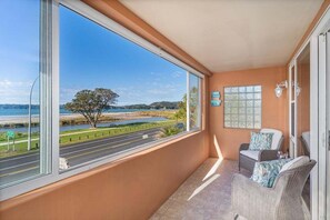 A balcony with a view of a road and water body, wicker furniture, and a wall-mounted sign. - Seaview Studio Apartment (Whitianga)