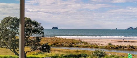 Vista di una spiaggia attraverso una finestra, con un prato in primo piano, un cartello e una costa in lontananza.