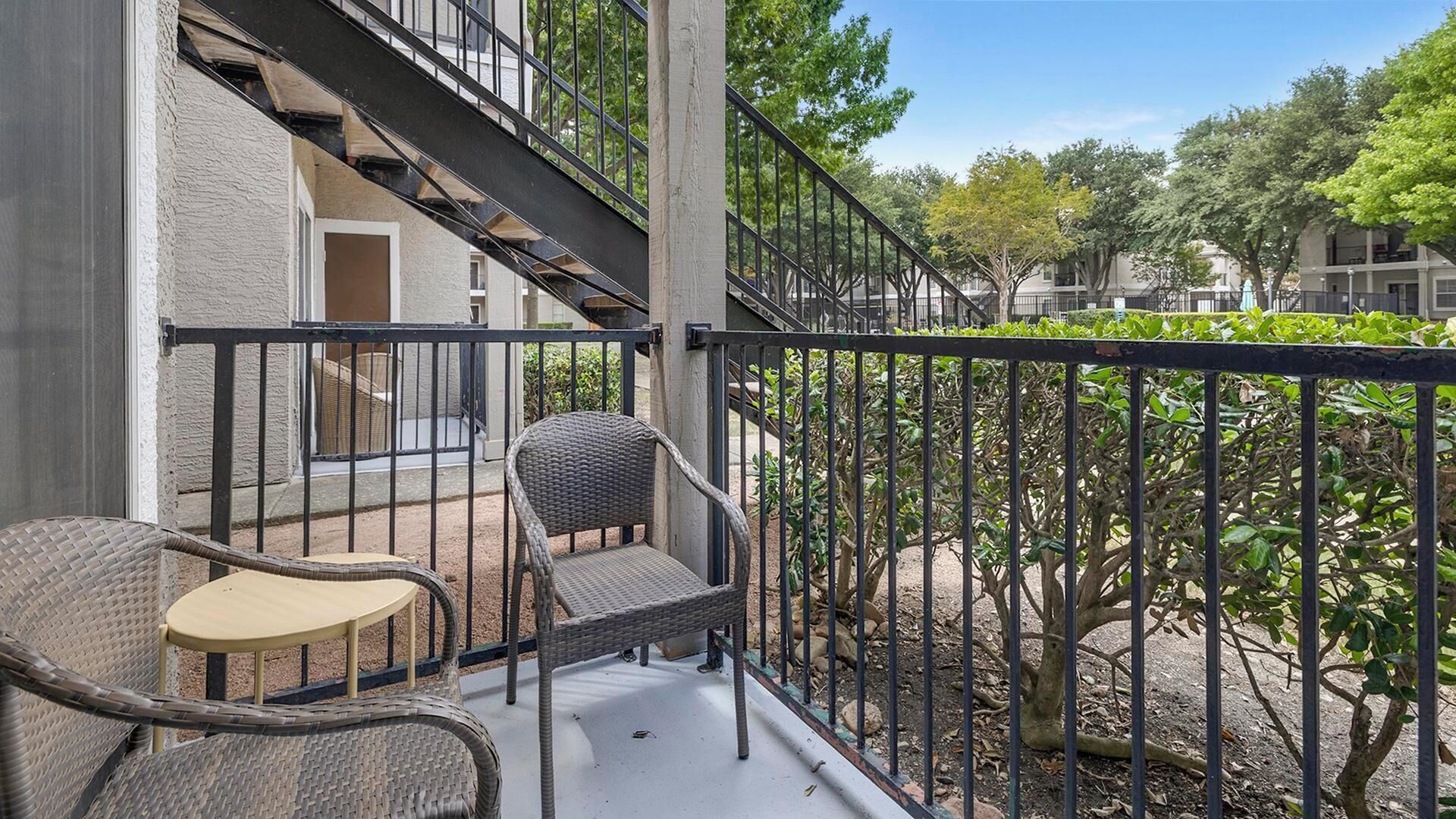 Un balcon doté de meubles en osier, d’une rambarde en métal et offrant une vue sur un immeuble avec un escalier.