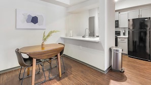 A modern kitchen with a black refrigerator, white cabinets, and a wooden dining table with chairs. - Landing | Spectacular 1BD, Courtyard, Gym (Allen)