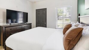 A bedroom with a bed, a dresser, a television, a door, and a window with blinds. - Landing | Spectacular 1BD, Courtyard, Gym (Allen)