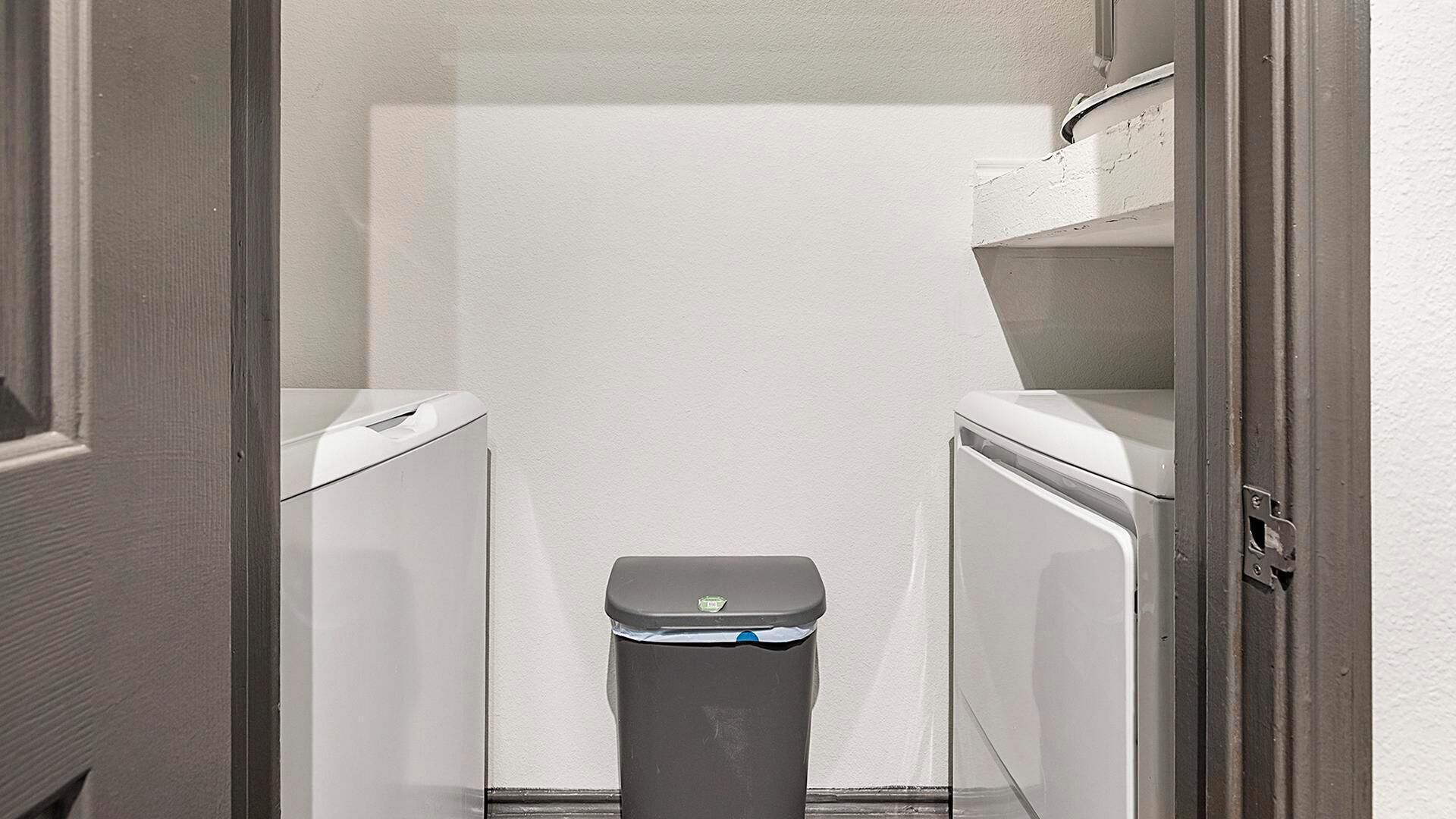 A narrow hallway with a trash bin in the center, flanked by two white appliances, likely a washer and dryer.