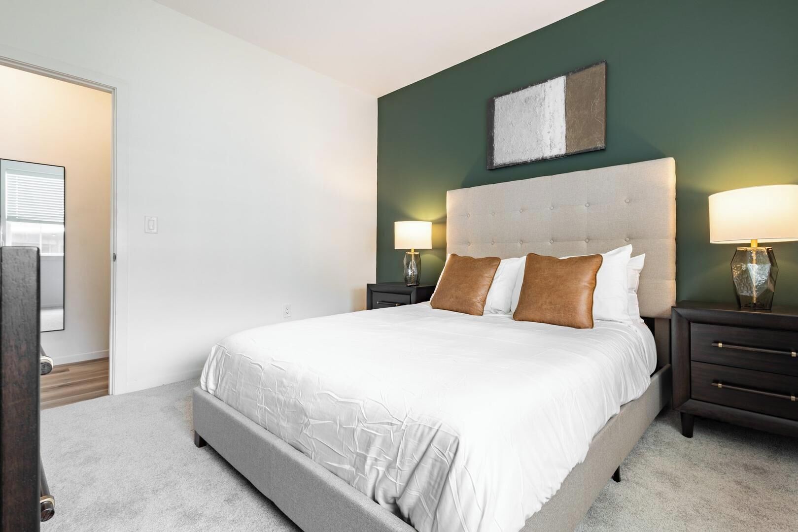 Une chambre à coucher avec un grand lit, deux tables de chevet avec des lampes, une tête de lit et une œuvre d’art accrochée au mur.
