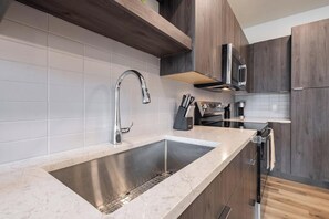 A modern kitchen with a stainless steel sink, a built-in oven, and wooden cabinets.