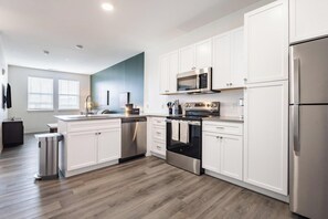A modern kitchen with white cabinetry, stainless steel appliances, and a wooden floor.