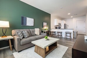 A modern living room with a sofa, coffee table, and a dining area with bar stools.