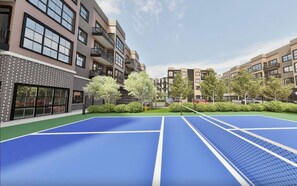 Ein Tennisplatz, umgeben von Mehrfamilienhäusern mit Balkonen und einer Ziegelaußenwand.