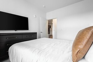 Ein Schlafzimmer mit einem Bett, einem an der Wand montierten Fernseher, einem Kleiderschrank und einer Tür zu einem anderen Raum.