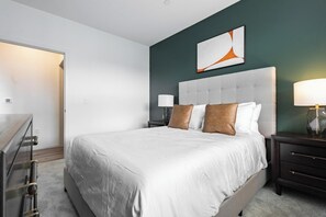 A bedroom with a large bed, two bedside tables, a nightstand, a wall-mounted lamp, and a door leading to another room. - Landing | Spectacular 1BD in Steelpointe Harbor (Bridgeport)