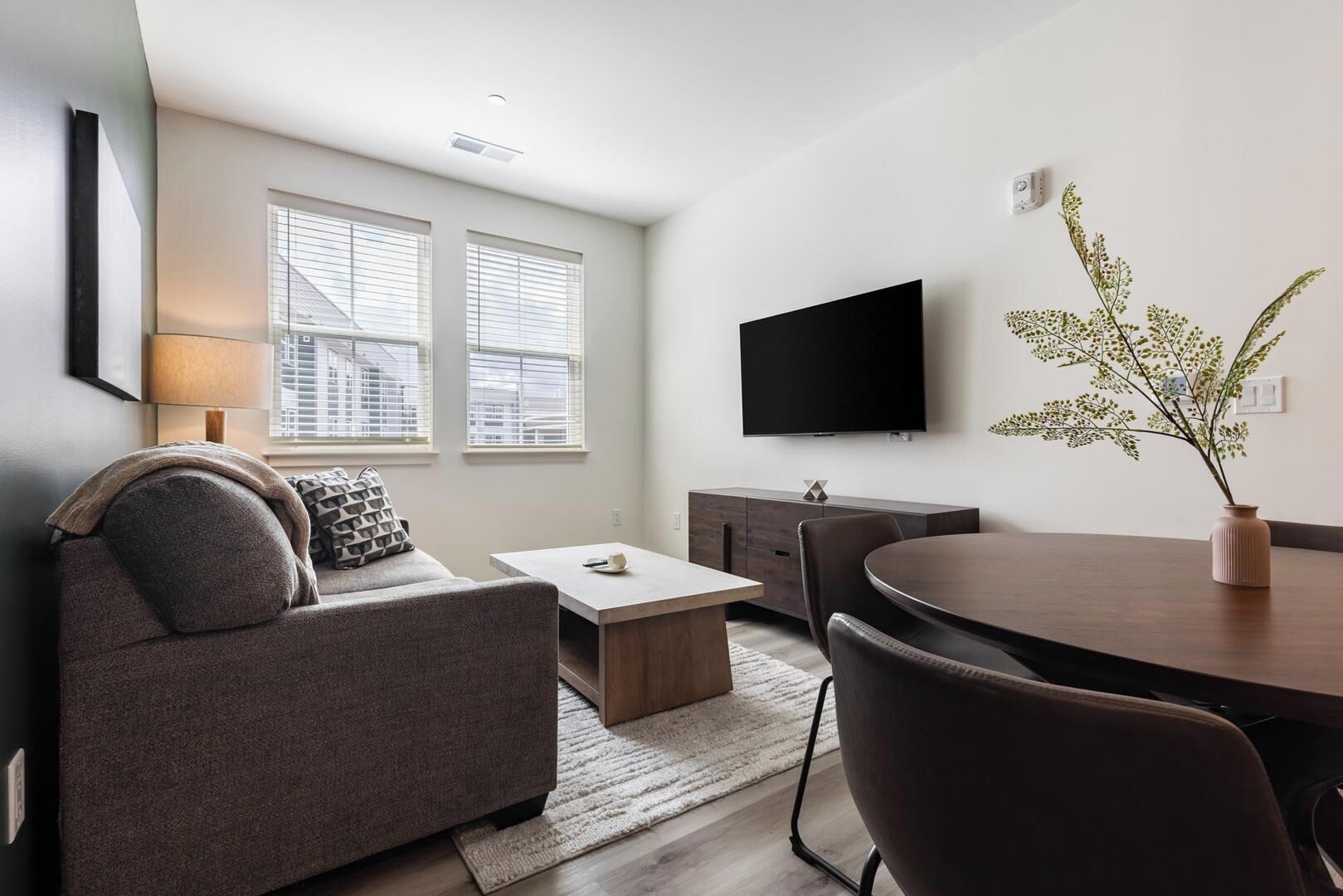 Un salon moderne comprenant un canapé, une table basse, une table à manger et un téléviseur à écran plat fixé au mur.