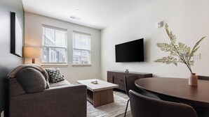 A modern living room with a sofa, coffee table, dining table, and a flat-screen TV mounted on the wall. - Landing | Spectacular 2BD in Steelpointe Harbor (Bridgeport)