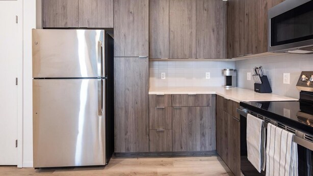 A modern kitchen with wooden cabinets, stainless steel appliances, and a black countertop. - Landing | Spectacular 2BD in Steelpointe Harbor (Bridgeport)