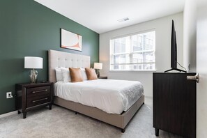 A bedroom with a bed, bedside tables, a nightstand, a window with blinds, and a wardrobe. - Landing | Spectacular 2BD in Steelpointe Harbor (Bridgeport)