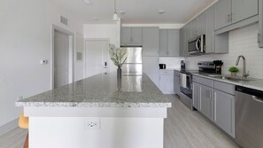 Eine moderne Küche mit Granit Arbeitsplatten, Edelstahlgeräten und grauen Schränken.