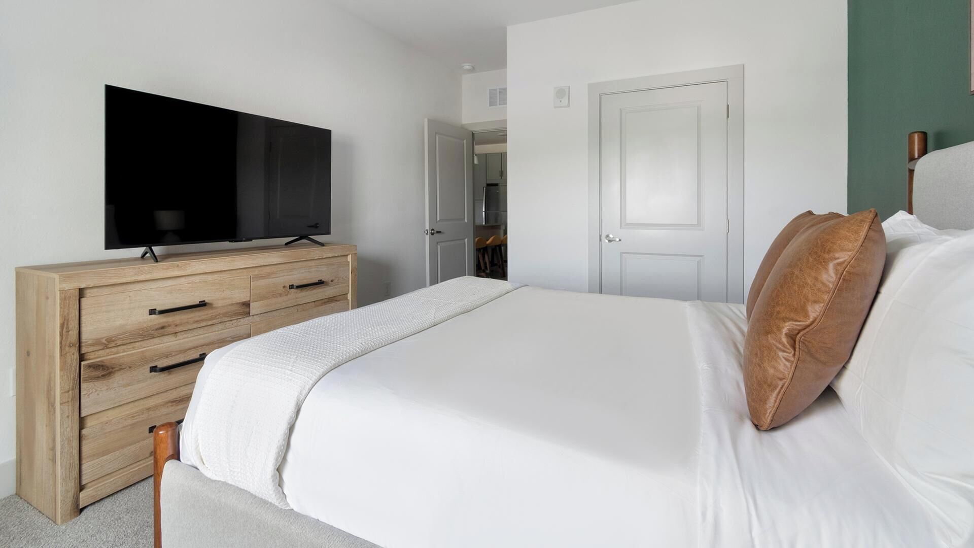 Un dormitorio con una cama, un televisor sobre un aparador de madera y una puerta que da a un baño.