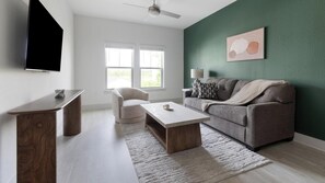 A living room with a sofa, a coffee table, a TV, and a ceiling fan. - Landing | Chic 1BD, Gym (St. Augustine)