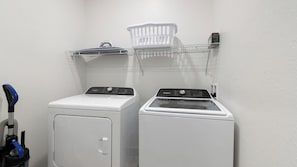 A laundry area with two front-loading washers and a dryer, a basket on a shelf, and a vacuum cleaner. - Landing | Modern 1BD, Gym (St. Augustine)