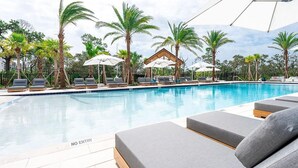 Un área de piscina con sillas de descanso y sombrillas, rodeada de palmeras.