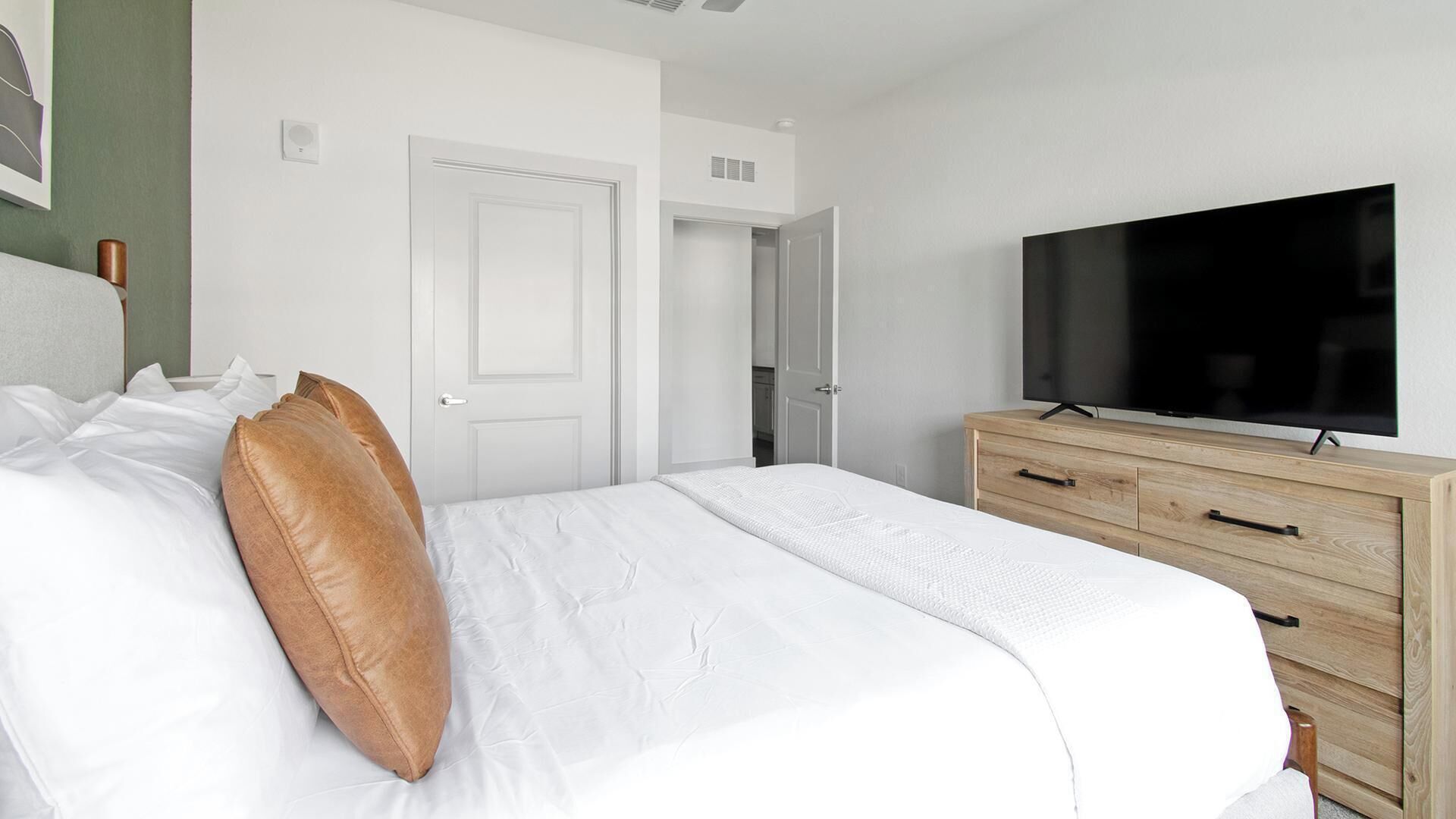 Habitació d'hotel amb un llit, una televisió, una petita arca de fusta i una porta blanca.