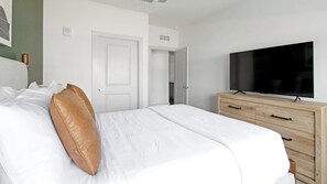 A hotel room with a bed, a television, a wooden dresser, and a white door. - Landing | Stylish 2BD, Gym (St. Augustine)