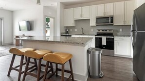 Une cuisine moderne avec des meubles blancs, des appareils en acier inoxydable, un comptoir en granit et des tabourets de bar en bois.