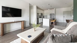 A modern living room with a flat-screen TV, a coffee table, a bench, and a sofa. - Landing | Stylish 2BD, Gym (St. Augustine)