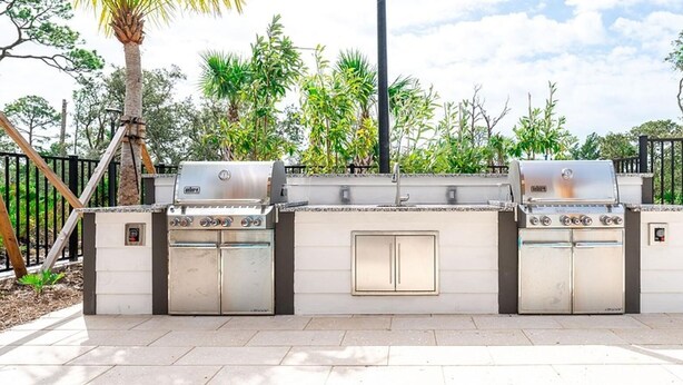 An outdoor kitchen with a gas stove, oven, and grill, surrounded by a fence and trees. - Landing | Amazing 1BD, Gym (St. Augustine)