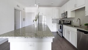 A modern kitchen with white cabinetry, stainless steel appliances, and a granite countertop. - Landing | Amazing 1BD, Gym (St. Augustine)
