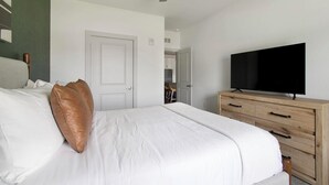 A hotel room with a bed, a television on a wooden dresser, and a door leading to another room. - Landing | Amazing 1BD, Gym (St. Augustine)