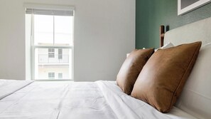 A hotel room with a bed, pillows, a window, and a view of buildings outside. - Landing | Stunning 1BD, Gym (St. Augustine)