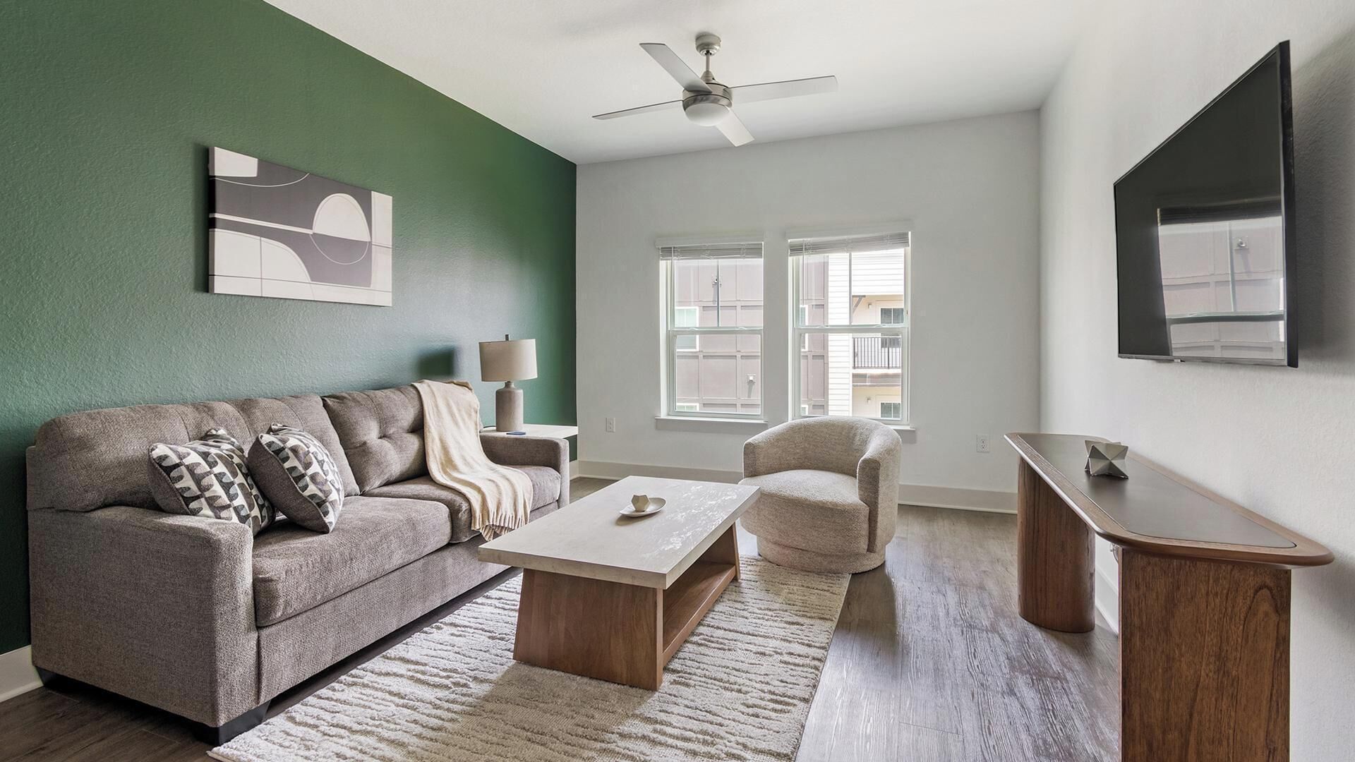 A living room with a sofa, armchair, coffee table, and a TV on a stand.