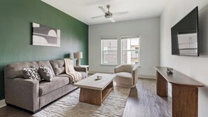 Ein Wohnzimmer mit Sofa, Sesseln, Couchtisch und Fernseher auf einem Schrank.