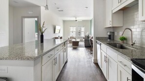 A modern kitchen with granite countertops, white cabinetry, and a built-in dishwasher. - Landing | Beautiful 1BD, Gym (St. Augustine)