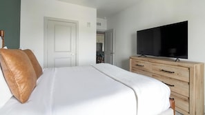 Ein Schlafzimmer mit einem Bett, einem Fernseher auf einer Holzkommode und einer Tür zu einem Badezimmer.
