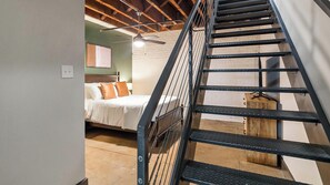 A bedroom with a bed, a wooden headboard, a ceiling fan, and a staircase with metal railings. - Landing | Stylish 1BD, Gym, Courtyard (Houston)