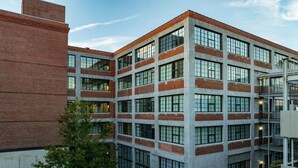 A multi-story building with a brick facade, large windows, and a courtyard with trees. - Landing | Spectacular 1BD, Gym, Courtyard (Houston)