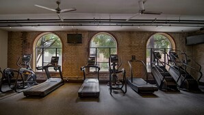 A gym with treadmills, elliptical machines, and weight stations, featuring large arched windows and exposed brick walls. - Landing | Spectacular 1BD, Gym, Courtyard (Houston)